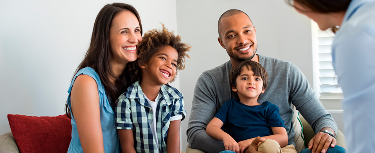 Happy young family sitting on couch and talking with family counselor. Smiling parents with adopted children discussing with counselor. Multiethnic family meeting a financial agent.